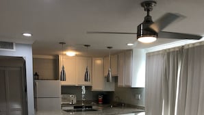 A modern kitchen with white cabinets, a central island with stools, a ceiling fan, and recessed lighting.