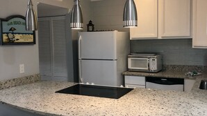 A kitchen with a granite countertop, white cabinets, a stainless steel refrigerator, a microwave, and a built-in oven. There are three bar stools with cushioned seats.