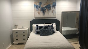 A bedroom with a bed, a nightstand, a painting, and a door.