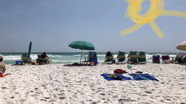 A beach with several beach chairs and umbrellas, a clear sky, and the ocean in the background.