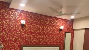 Une chambre à coucher avec un grand lit, deux tables de chevet, un ventilateur de plafond et un papier peint à motifs.