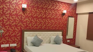 Relax in a spacious room with a large bed, tufted headboard, and two pillows, surrounded by a red patterned wallpaper and a ceiling fan.
