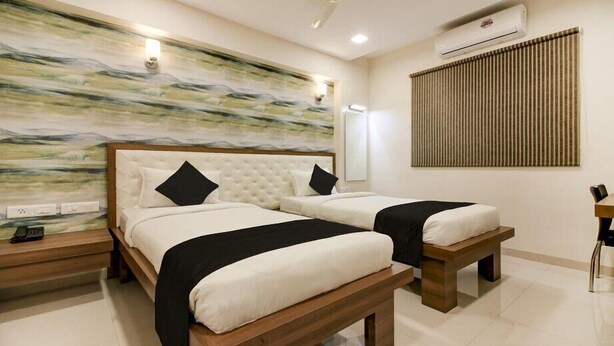 Une chambre d’hôtel avec deux lits, une tête de lit en bois, un climatiseur fixé au mur et un grand tableau abstrait.