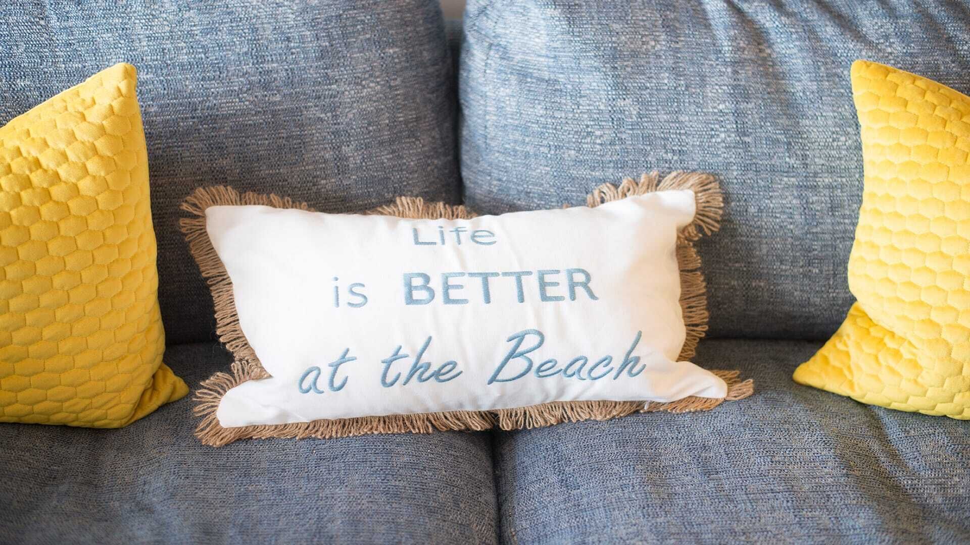 Un sofá con un cojín que dice 'La vida es MEJOR en la playa'.