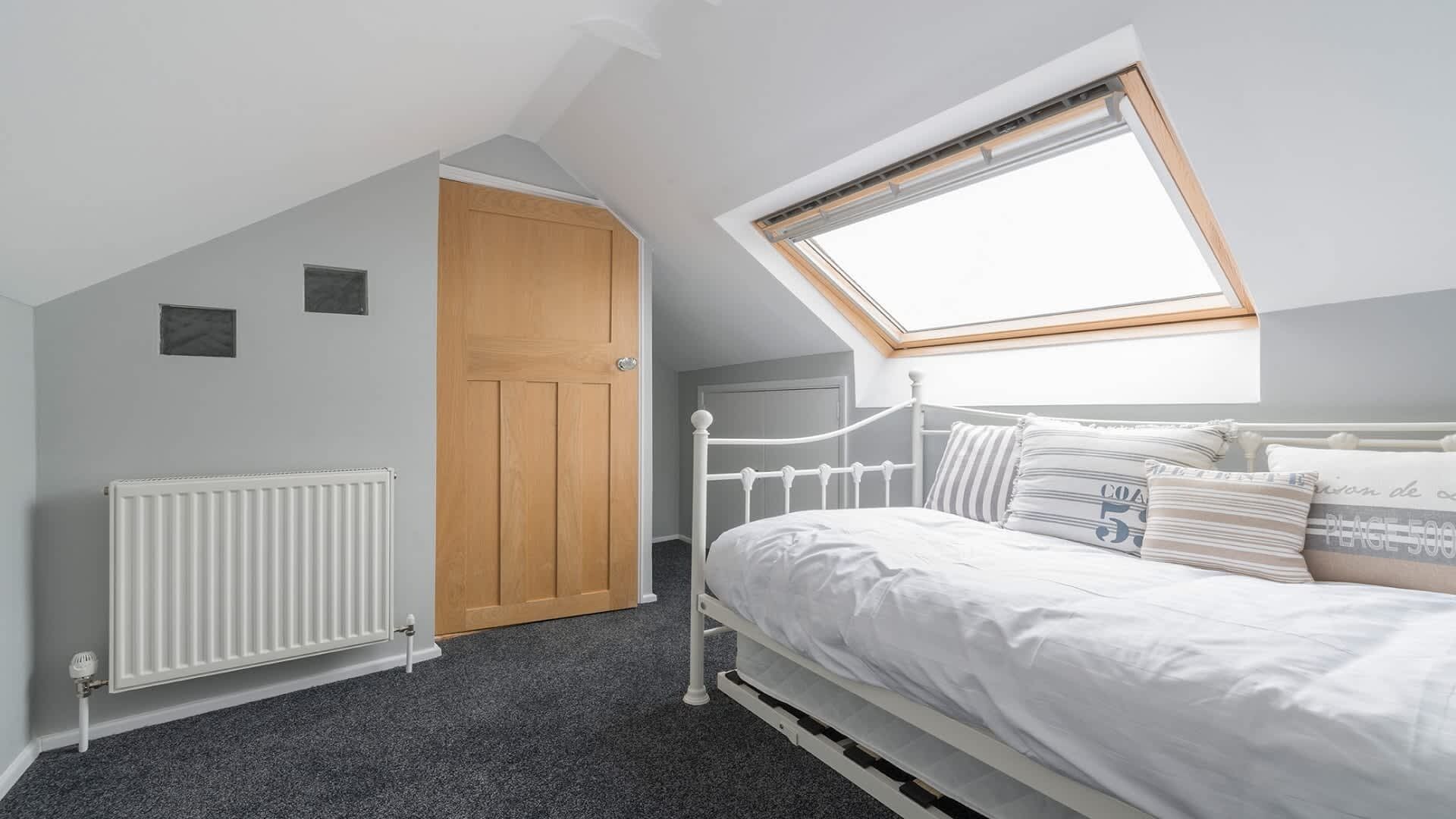 A bedroom with a sloped ceiling, a skylight, a white radiator, a wooden door, and a white metal bed frame.