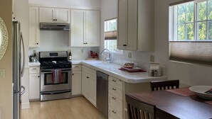 A kitchen with white cabinets, a stainless steel stove, and a wooden dining table with chairs. - Coastal Studio Retreat!! WALK TO SURF & SAND or 1 MIN DRIVE!!! GREAT LOCATION!!! (Carlsbad)