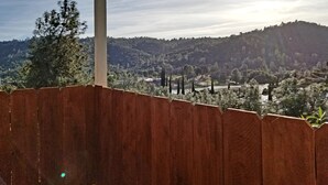A view from a covered outdoor area with a wooden fence, overlooking a hilly landscape with trees and a road. - The Cottage on Campbell- In town studio with a view!  (Mariposa)