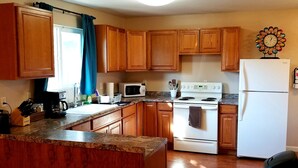 A kitchen with wooden cabinets, a white refrigerator, a stove, and a microwave. - The Cottage on Campbell- In town studio with a view!  (Mariposa)