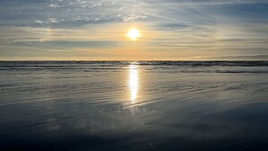 Une plage où le soleil se reflète sur l’eau, un ciel dégagé et un horizon lointain.