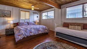 Une chambre avec un plafond en bois, deux lits, une table de chevet, une lampe et une fenêtre avec des stores.