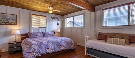 A bedroom with a wooden ceiling, two beds, a nightstand, a lamp, and a window with blinds.