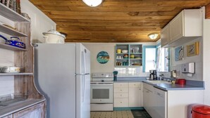 Une cuisine équipée d’un réfrigérateur, d’un four et d’un évier, avec un plafond en bois et un sol carrelé.