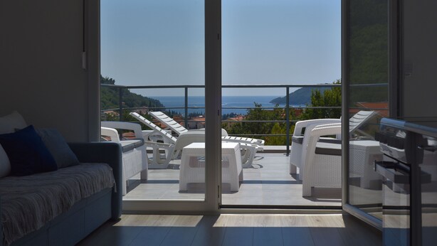 Ein Balkon mit weißen Korbmöbeln, einer Couch und Blick auf das Meer und die Hügel.