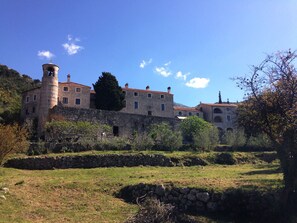 A historic stone building with a tower, surrounded by a stone wall and lush greenery.