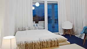Ein Hotelzimmer mit einem großen Bett, einem Sessel, einem Schreibtisch und Blick ins Freie.