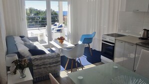 Ein modernes Wohnzimmer mit einer Couch, Sesseln, einem Esstisch und einer Küchenzeile mit Herd und Schränken.