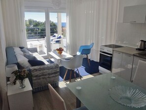 A modern living room with a sofa, chairs, a dining table, and a kitchen area with a stove and cabinets.