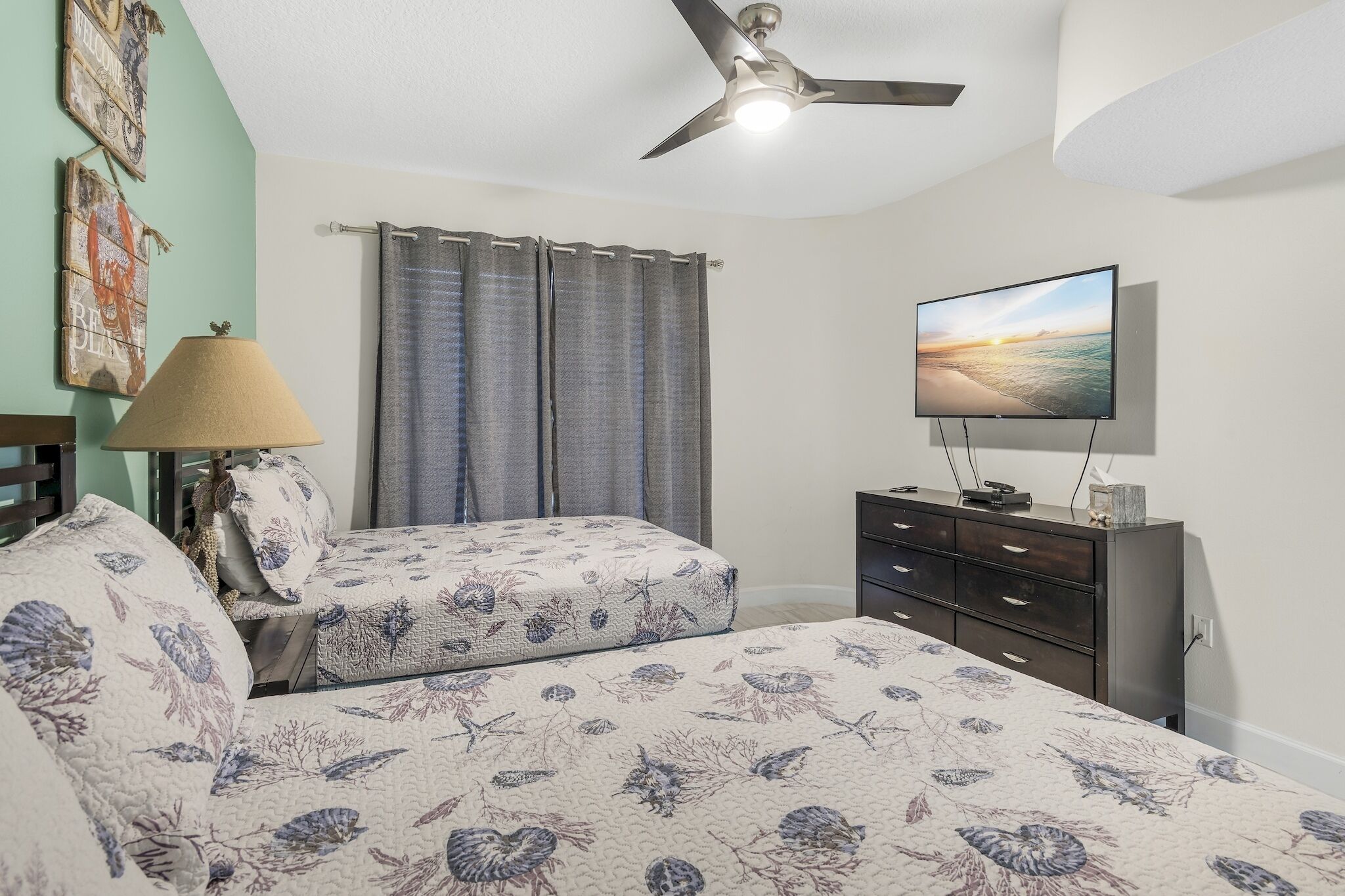Un dormitorio con una cama, televisión, ventilador de techo, cortinas y cómoda.