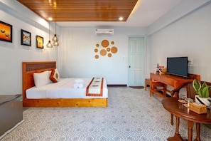 A hotel room with a wooden bed, a desk with a television, a small table with a plant, and a patterned floor. - Casamia Hoi An Villa (Da Nang)