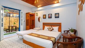 Une chambre d’hôtel avec deux lits, un plafond en bois, un coin repas avec une table et des chaises, et une vue sur un jardin par une porte ouverte.