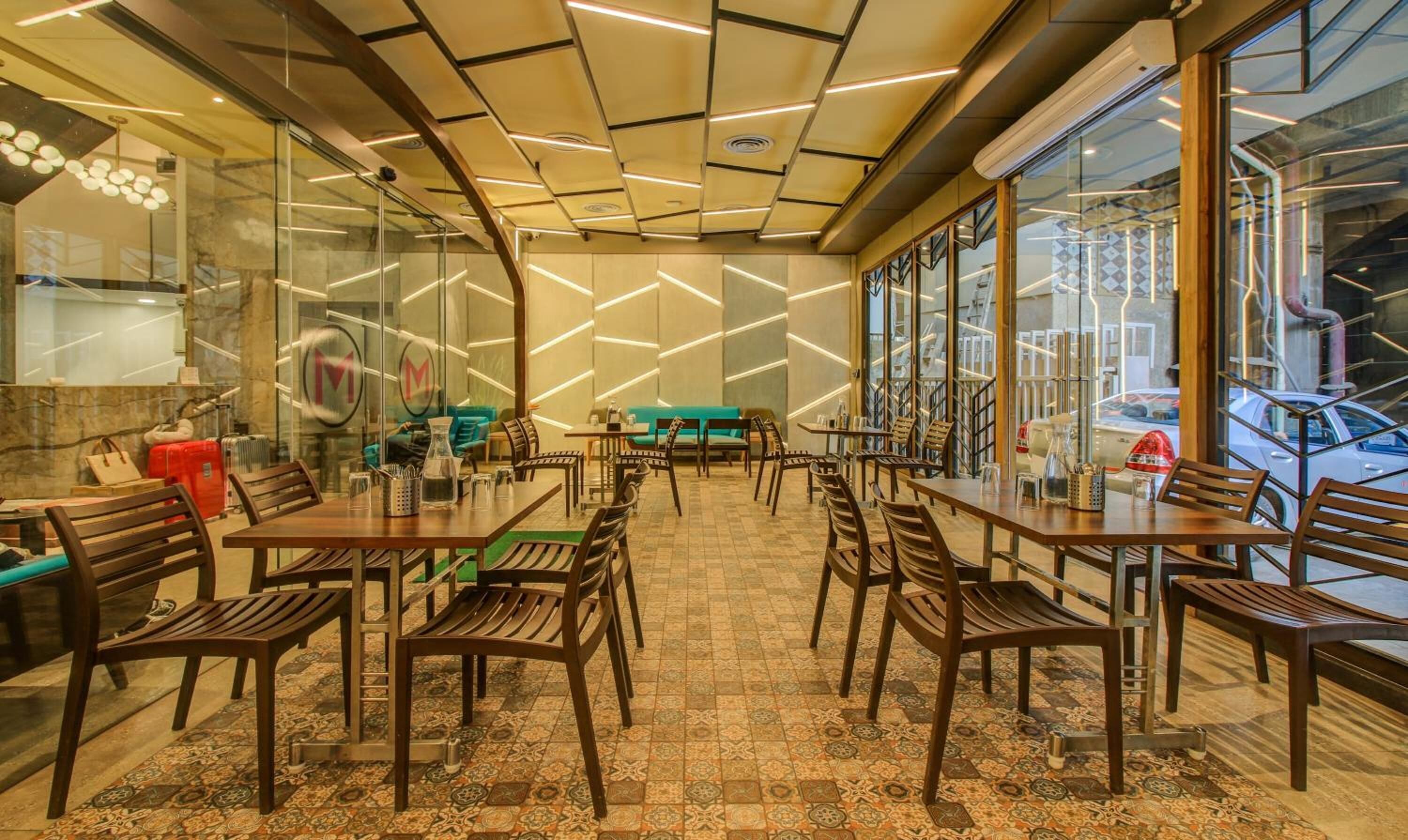A restaurant with a modern interior, featuring a mix of wooden and metal furniture, a patterned tile floor, and a unique ceiling design with linear lighting.