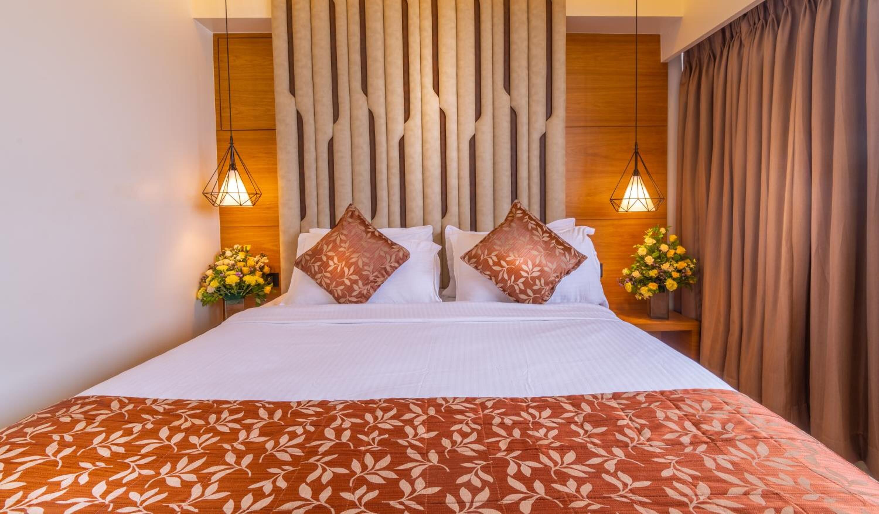 A hotel room with a large bed, two bedside tables with lamps, a wooden headboard, and floral arrangements.