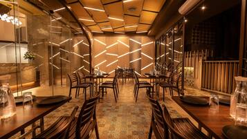 Un restaurante con un interior moderno, que presenta un suelo estampado, mesas y sillas de madera, y un techo decorativo con iluminación lineal.