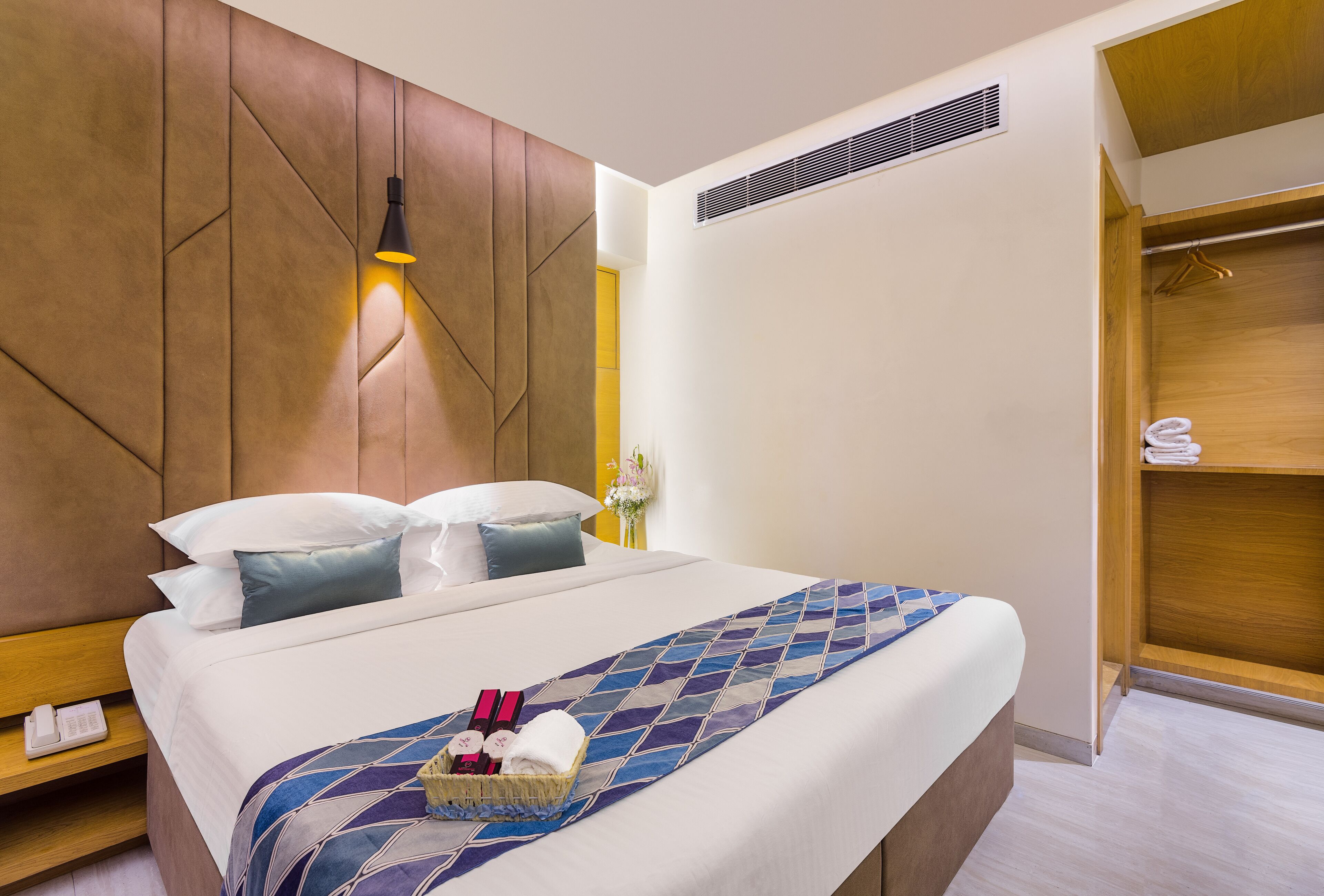 Habitación de hotel con una cama grande, una mesita de noche con teléfono, una lámpara de pared, un armario de madera y un baño con perchero.