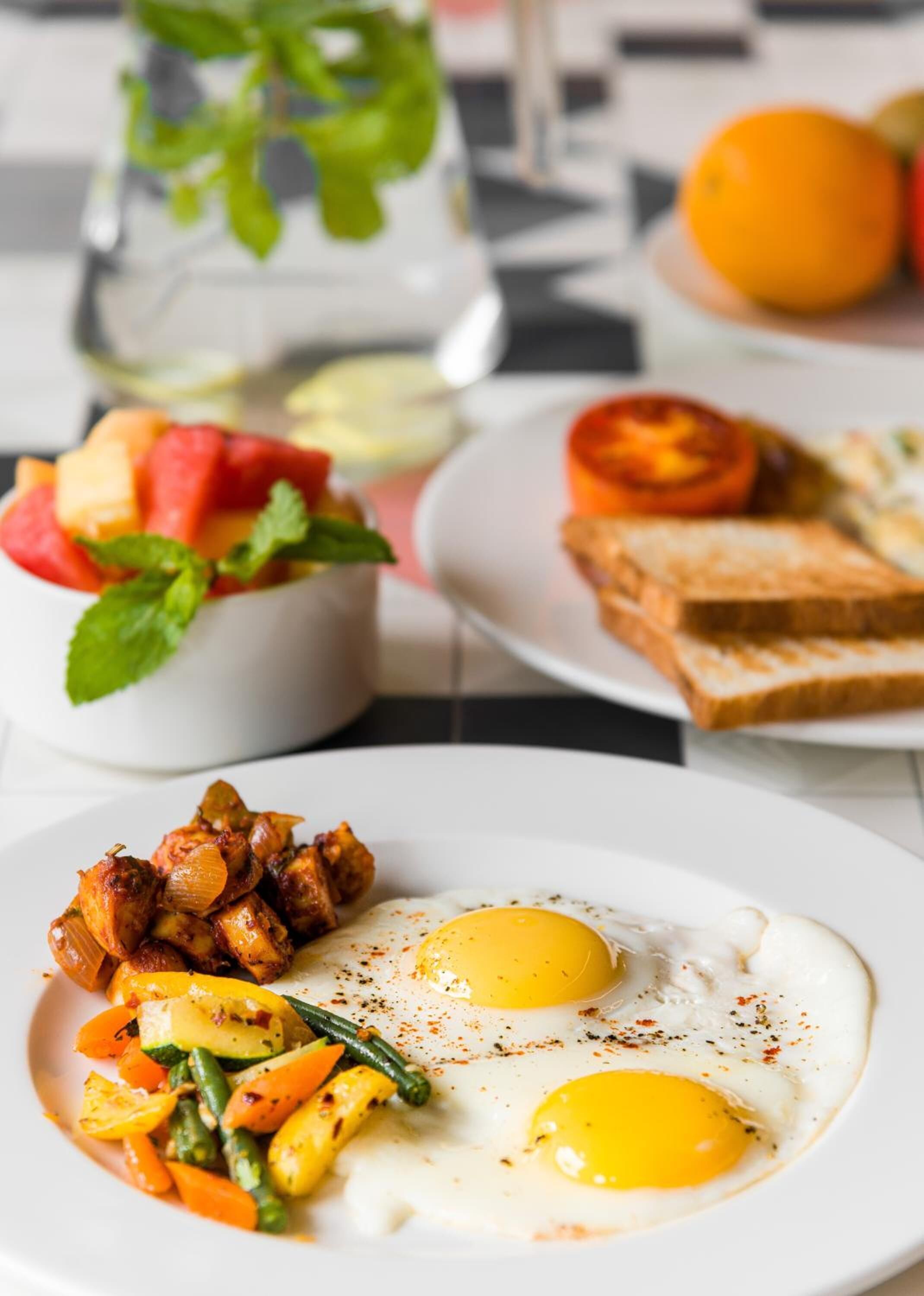 Ein Frühstückstisch mit Eiern, Gemüse, Toast und einer Schüssel Obstsalat.