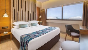 Hotelkamer met een groot bed, een bureau, een stoel, een raam met uitzicht en een plafondventilator.