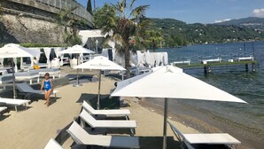 A lakeside resort with sun loungers, umbrellas, and a view of the lake and hills. - Secret Garden Art Museum (Arona)