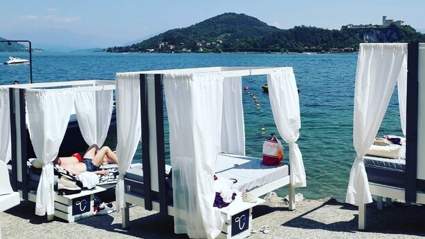 A row of four white canopy beds with a view of a calm sea and a distant hill. - Secret Garden Art Museum (Arona)