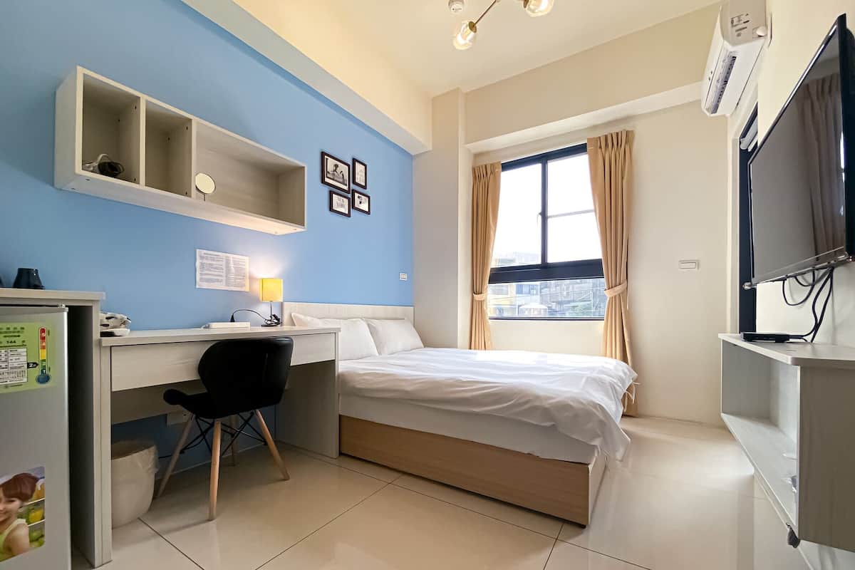 A hotel room with a bed, desk, chair, and a window with curtains.