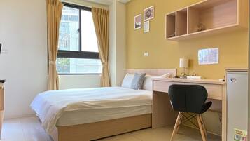 A hotel room with a bed, desk, chair, and a small refrigerator.