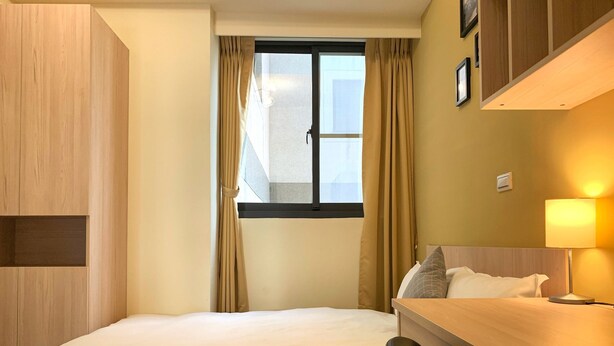 A hotel room with a bed, a desk, a chair, a window with curtains, and a lamp. - Adagio Hostel (Taichung)