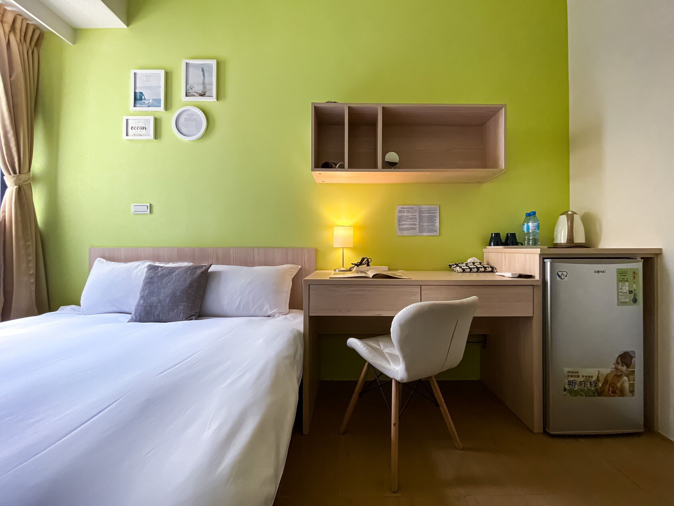 Une chambre d’hôtel équipée d’un lit, d’un bureau, d’une chaise, d’un réfrigérateur et d’une étagère avec une lampe.