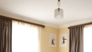 A hotel room with two single beds, a wooden floor, a chandelier, and a large window with curtains.