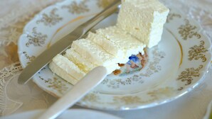 A plate with a white and gold design, containing a piece of white food, possibly tofu, and a knife. - Seva Guesthouse in Byurakan (Byurakan)