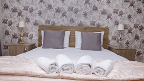 A neatly made bed with a headboard, two bedside tables with lamps, and floral wallpaper. - Seva Guesthouse in Byurakan (Byurakan)
