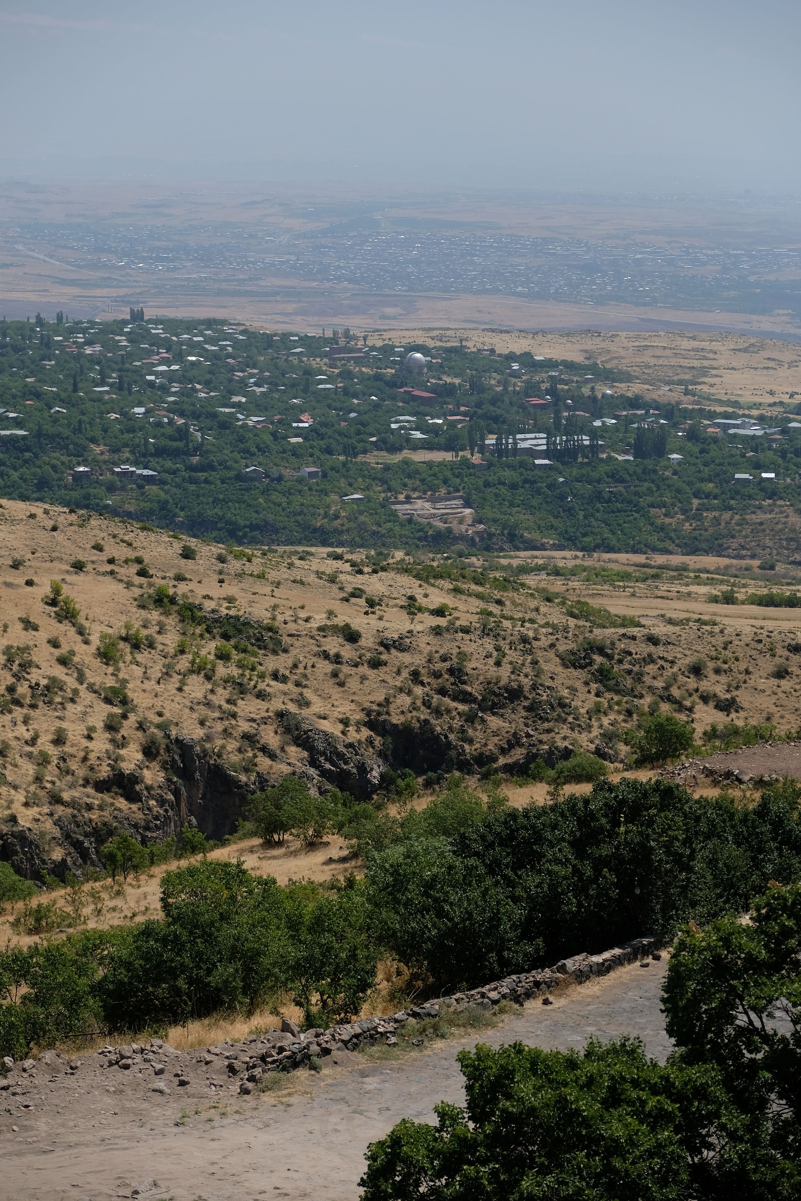 A hilly landscape with sparse vegetation and a distant view of a town.