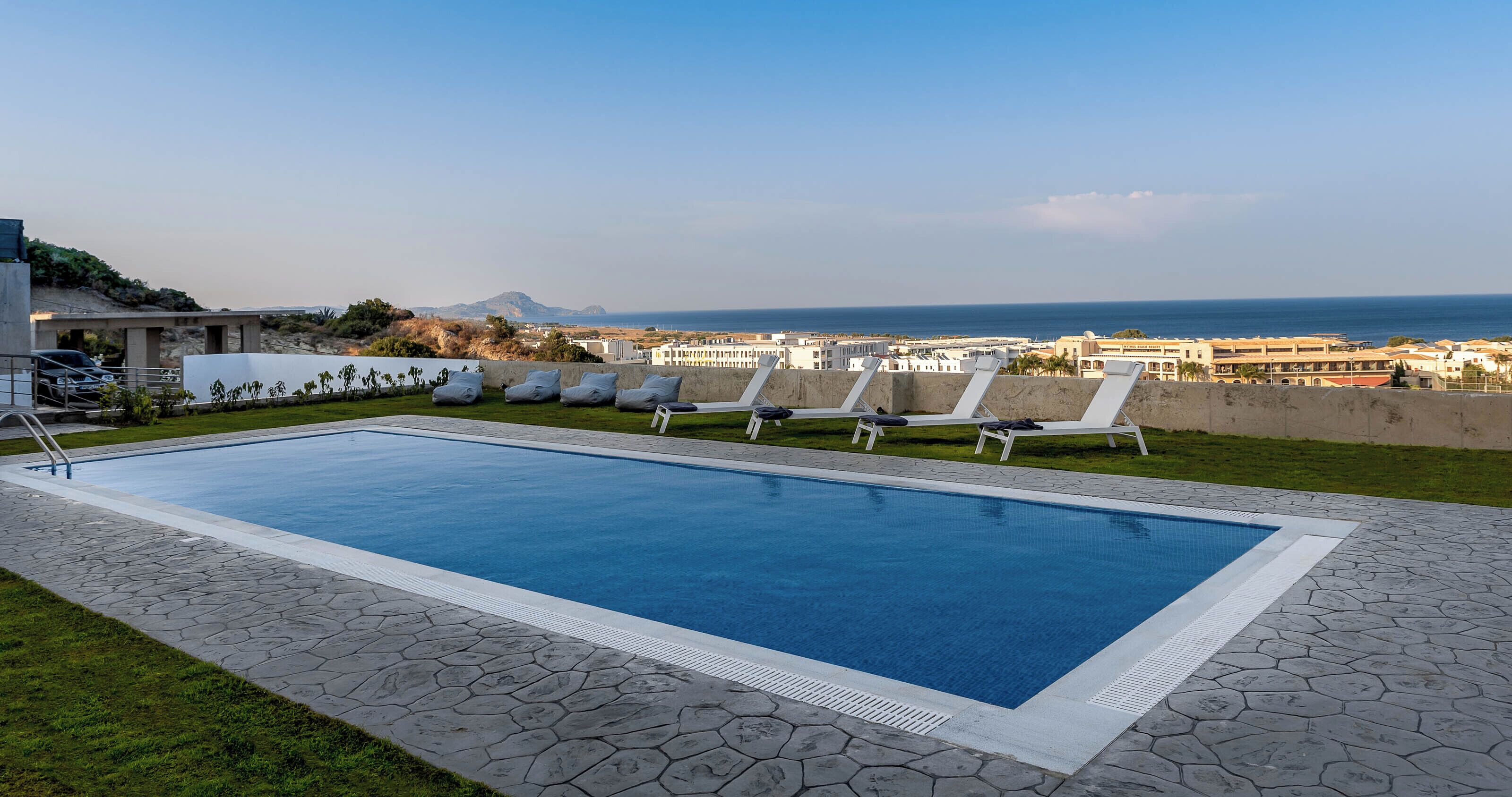 Una piscina con sillones de descanso, vista despejada al mar y una montaña distante.