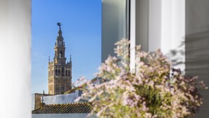 A window view of a building with a tower, a vase with flowers, and a framed picture on a shelf. - Genteel Home Santa Teresa VI (Sevilla)