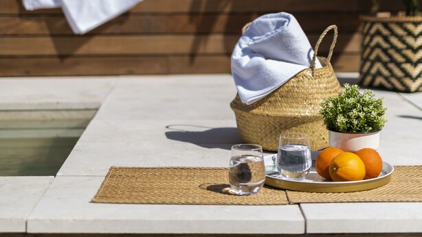 A table with a woven basket, a small potted plant, a plate with oranges, and two glasses of water. - Genteel Home Santa Teresa VI (Sevilla)