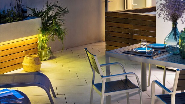 Une terrasse avec une table et des chaises, un banc en bois, une plante en pot et une vue sur une tour.