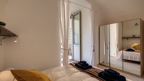 Un dormitorio con cama, espejo, armario y ventana con cortinas.