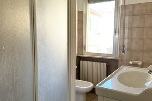 A bathroom with a toilet, a bidet, a sink, a window, and a radiator. - M223 - Marcelli, three-room apartment in the center and facing the sea (Marcelli)