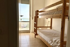Une chambre avec des lits superposés, une porte donnant sur un balcon, un plancher en bois et une vue sur l’extérieur.
