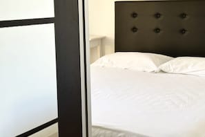 A bed with a tufted headboard, white bedding, and a partial view of a white wall and a dark-colored door frame.
