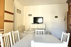 A dining area with a white table, white chairs, a television on a cabinet, and a radiator.
