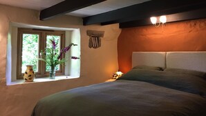 Een slaapkamer met een bed, een raam met uitzicht, een vaas met bloemen en een wandlamp.